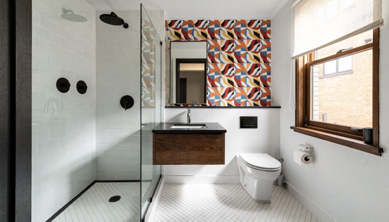 Renovated primary suite bathroom in a Vancouver home: dark tile, frameless glass shower, and warm brass fixtures.