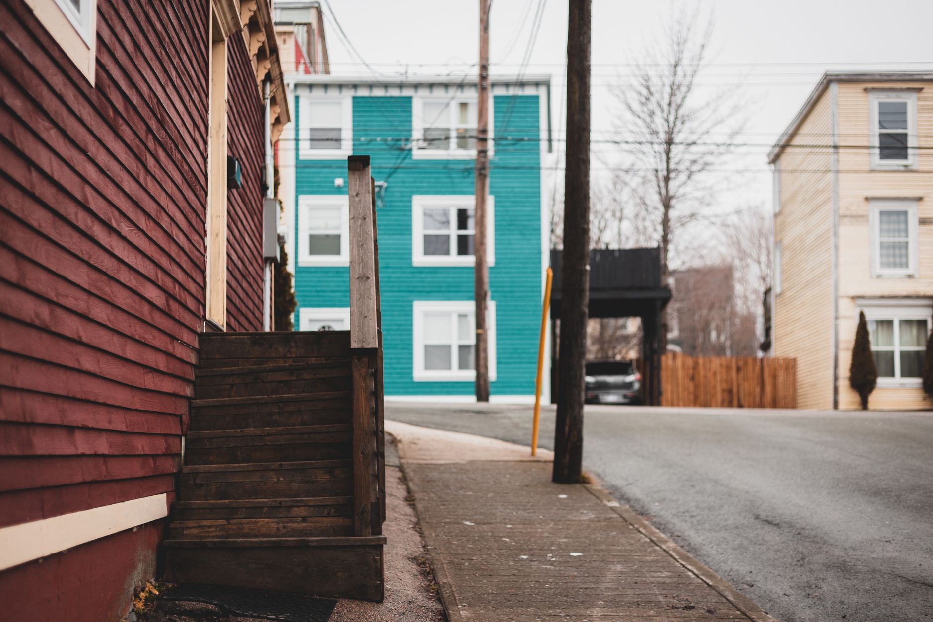 Shabby stairs of residential building located on sidewalk near asphalt road on street with tall pole and houses of town