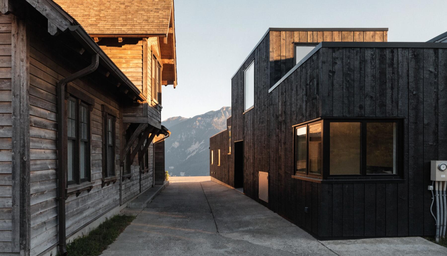 Vancouver back lane with completed modern black cedar laneway house behind a character craftsman home, coastal mountains in background