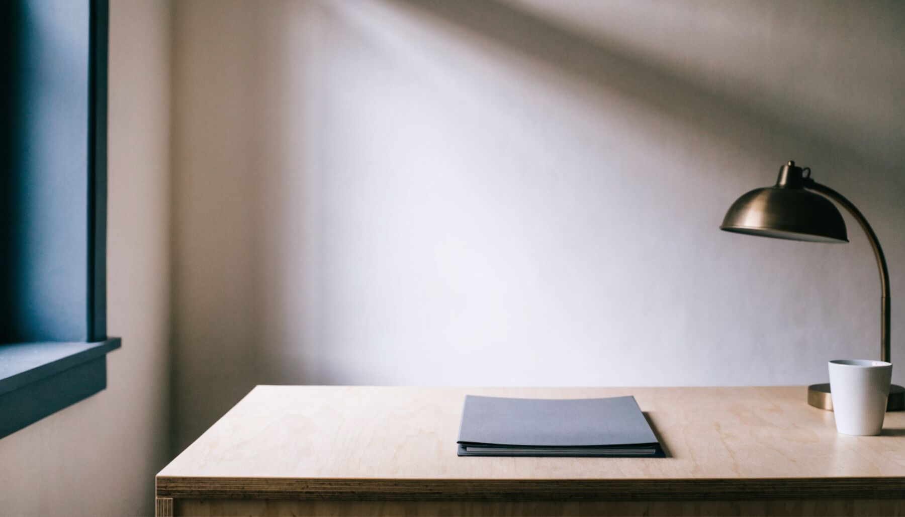 Quiet contractor office desk in warm daylight with a closed folder and a bronze desk lamp