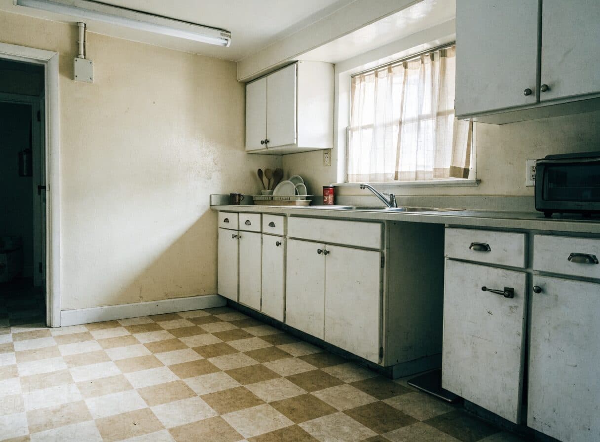 Dated 1970s Vancouver rental apartment kitchen before renovation, showing original laminate countertop and melamine cabinets