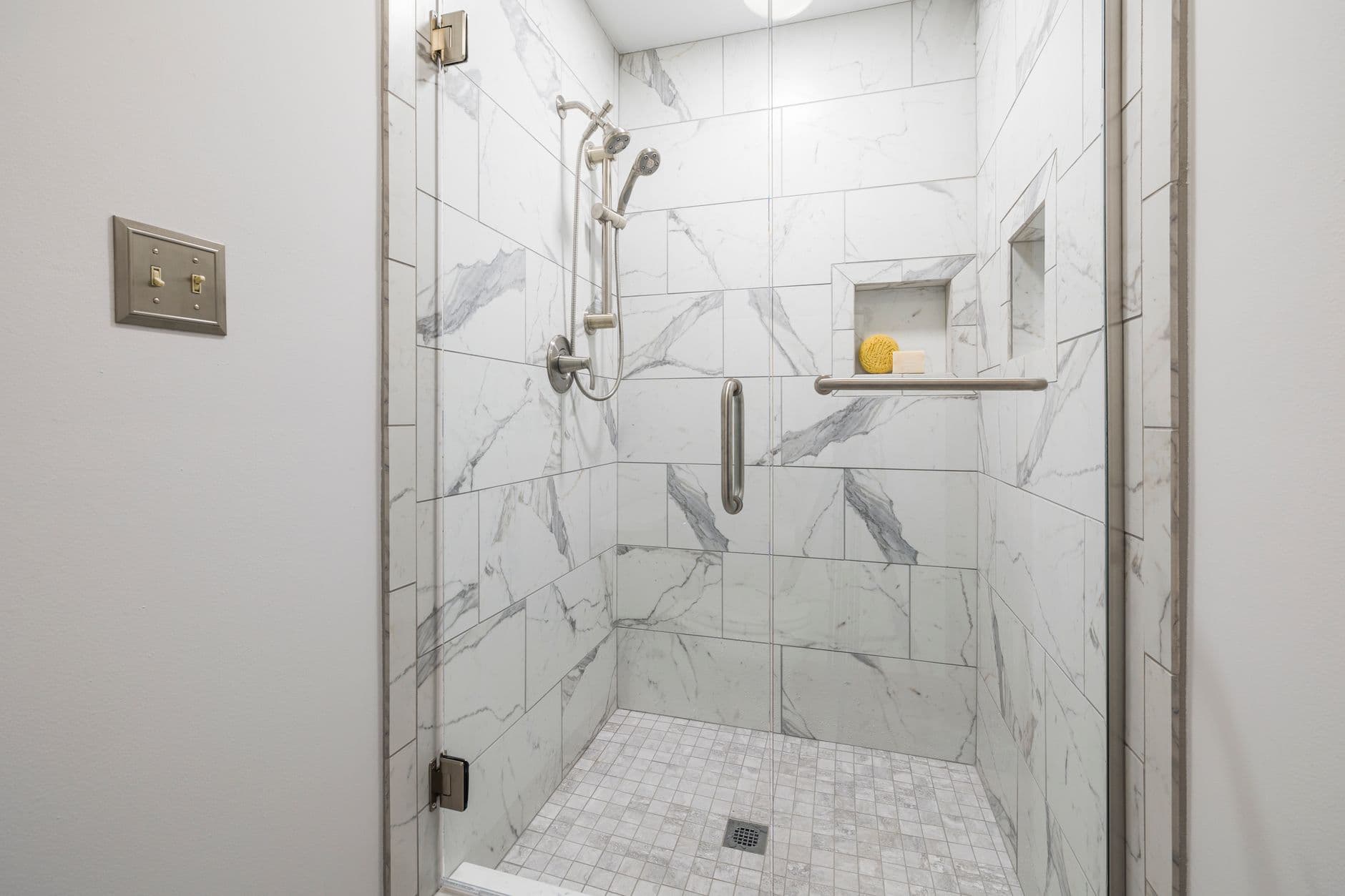 Elegant bathroom with white marble tiles and glass door, showcasing modern interior design.